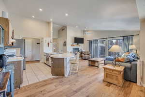 Kitchen featuring light countertops, light wood-type flooring, open floor plan, a peninsula, and high vaulted ceiling