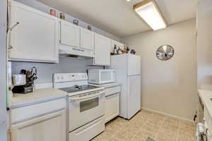 Kitchen with white appliances, light countertops, white cabinets, and under cabinet range hood
