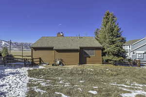 Snow covered house with a shingled roof, a chimney, and a wooden deck
