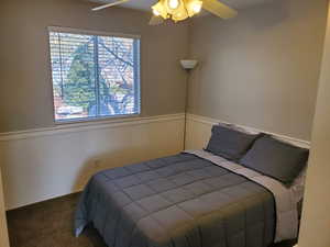 Carpeted bedroom featuring wainscoting and a ceiling fan