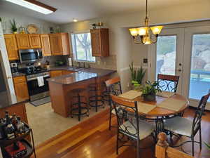 Kitchen with brown cabinets, pendant lighting, appliances with stainless steel finishes, dark stone countertops, and a kitchen breakfast bar