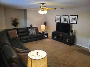 Carpeted living room featuring ceiling fan and baseboards