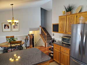 Kitchen featuring freestanding refrigerator, brown cabinetry, a chandelier, light wood-style flooring, and hanging light fixtures