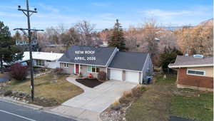View of front facade with concrete driveway, roof with shingles, a garage, and a front lawn