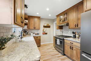 Kitchen with appliances with stainless steel finishes, brown cabinetry, light countertops, light wood finished floors, and recessed lighting