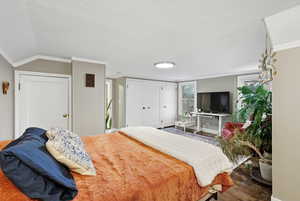 Bedroom featuring ornamental molding, two closets, wood finished floors, and lofted ceiling