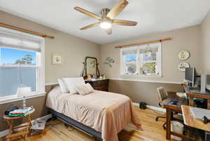 Bedroom with a desk, light wood-style flooring, and ceiling fan