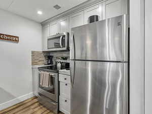 Kitchen featuring appliances with stainless steel finishes, light wood-type flooring, tasteful backsplash, light stone countertops, and recessed lighting