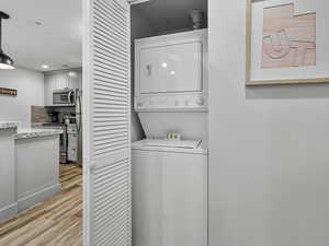 Laundry area with light wood-type flooring, recessed lighting, and stacked washer / dryer