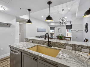 Kitchen with stainless steel dishwasher, hanging light fixtures, light stone counters, open floor plan, and recessed lighting