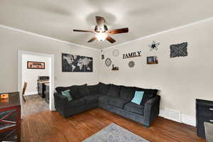 Living area featuring dark wood-style flooring, ceiling fan, and ornamental molding