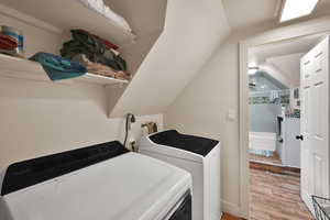 Washroom with light wood-type flooring, washer and clothes dryer, and lofted ceiling