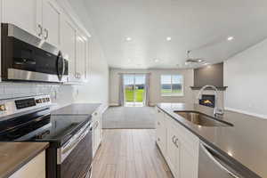 Kitchen with stainless steel appliances, white cabinetry, a glass covered fireplace, dark stone countertops, and recessed lighting