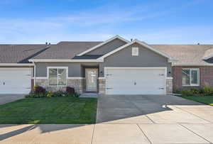 View of front of house with stone siding, stucco siding, a front lawn, an attached garage, and concrete driveway