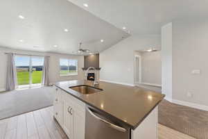 Kitchen featuring open floor plan, white cabinets, dishwasher, a glass covered fireplace, and a center island with sink