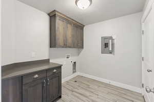 Washroom featuring cabinet space, light wood-style flooring, a textured ceiling, electric panel, and hookup for a washing machine