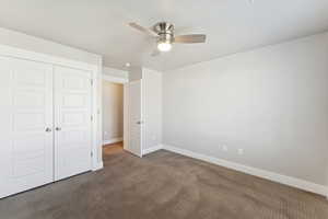 Unfurnished bedroom featuring a closet, ceiling fan, and dark carpet