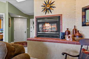 Living room featuring a textured wall, a tiled fireplace, and vaulted ceiling