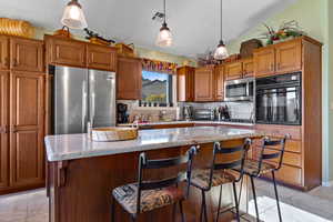 Kitchen featuring appliances with stainless steel finishes, tasteful backsplash, light stone counters, light tile patterned flooring, and vaulted ceiling