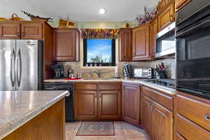 Kitchen with black appliances, brown cabinets, light tile patterned flooring, a textured ceiling, and tasteful backsplash