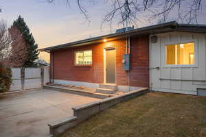 Back of property at dusk featuring a gate, a yard, and brick siding