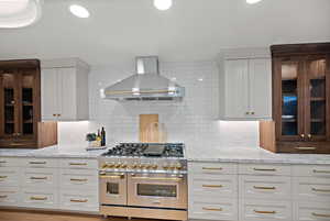 Kitchen with double oven range, wall chimney exhaust hood, white cabinetry, light stone counters, and recessed lighting