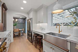 Kitchen with hanging light fixtures, light stone countertops, white cabinets, recessed lighting, and wallpapered walls