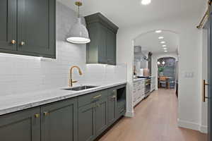 Kitchen featuring light stone counters, arched walkways, wall chimney range hood, recessed lighting, and tasteful backsplash