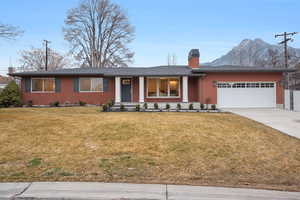 Ranch-style home featuring a porch, a front yard, a chimney, and driveway