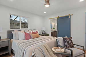 Bedroom with a barn door, ceiling fan, ensuite bathroom, recessed lighting, and wood finished floors