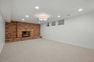 Finished below grade area featuring a brick fireplace, light carpet, and recessed lighting