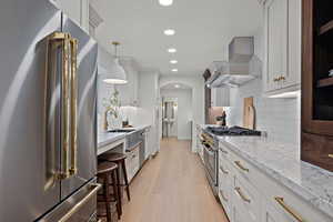 Kitchen with high end appliances, arched walkways, light wood finished floors, recessed lighting, and hanging light fixtures