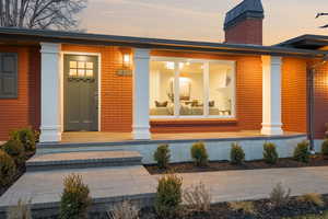 Exterior entry at dusk featuring brick siding, a chimney, and covered porch