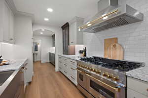 Kitchen with island range hood, double oven range, light stone counters, light wood-type flooring, and recessed lighting