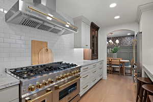 Kitchen with ventilation hood, stainless steel appliances, recessed lighting, light stone countertops, and light wood-type flooring
