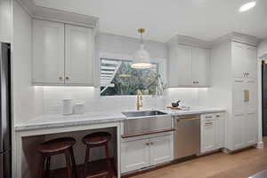 Kitchen featuring light stone counters, pendant lighting, tasteful backsplash, stainless steel appliances, and light wood-style flooring