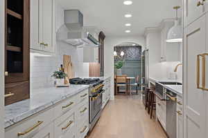Kitchen featuring light stone countertops, high quality appliances, light wood finished floors, wall chimney range hood, and recessed lighting
