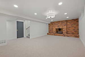 Finished below grade area with light colored carpet, recessed lighting, a fireplace, stairs, and brick wall