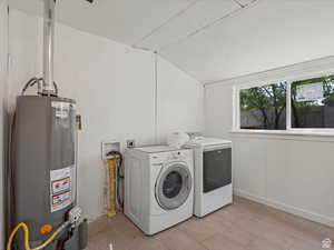 Laundry room featuring water heater, wood walls, washing machine and dryer, lofted ceiling, and wood finished floors
