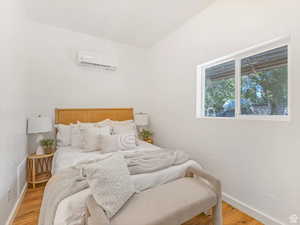 Bedroom with a wall mounted AC and wood finished floors
