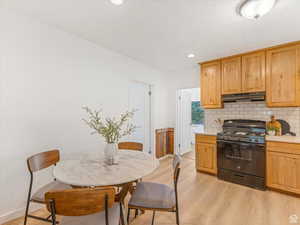 Kitchen with gas stove, light wood finished floors, under cabinet range hood, backsplash, and recessed lighting