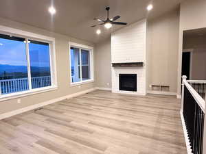Unfurnished living room with a ceiling fan, a mountain view, light wood-style flooring, a large fireplace, and recessed lighting