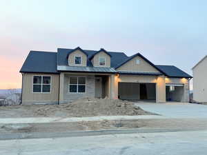 View of front of house with board and batten siding, driveway, covered porch, a garage, and a metal roof