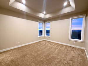 Carpeted empty room featuring a raised ceiling and baseboards