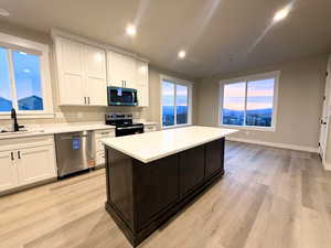 Kitchen featuring white cabinetry, appliances with stainless steel finishes, light wood-type flooring, vaulted ceiling, and recessed lighting