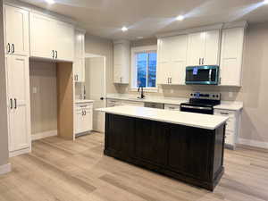 Kitchen with appliances with stainless steel finishes, a kitchen island, white cabinetry, light wood-style flooring, and recessed lighting