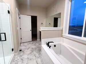 Bathroom featuring a shower stall, a garden tub, and light marble finish flooring