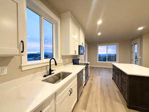 Kitchen featuring white cabinets, light wood finished floors, black appliances, recessed lighting, and light stone counters