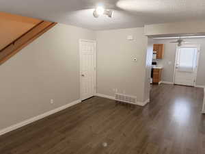 Unfurnished living room featuring a ceiling fan, dark wood finished floors, and a textured ceiling
