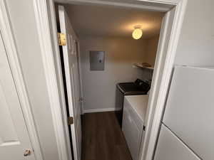 Washroom with a textured ceiling, dark wood finished floors, electric panel, and washing machine and clothes dryer